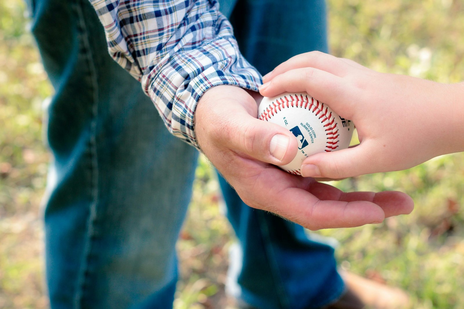 A close-up of a father and son passing a baseball outdoors on a sunny day.